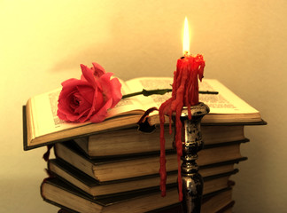 Old books, red rose and a candle in sepia tone