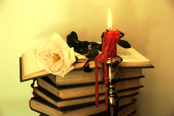 Old books, red rose and a candle in sepia tone