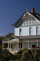 A blue and grey house, white trellis work, thin windows, bushes