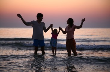 Father with mother hold child in sea on sunset