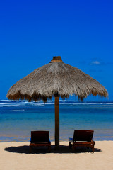 Two beach chairs under awning near ocean