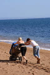 Fototapeta na wymiar Two women pushing a pram on a beach