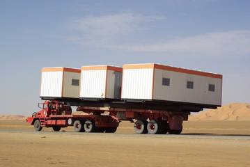 camion rouge transportant trois maisons préfabriquées