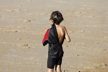 petit garçon qui enfile sa combinaison de surf sur la plage