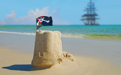 Fototapeta na wymiar Sand castle on beach with pirate flag and clipper ship