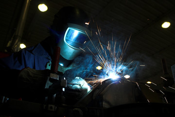 Welder welding a metal part in an industrial environment - obrazy, fototapety, plakaty