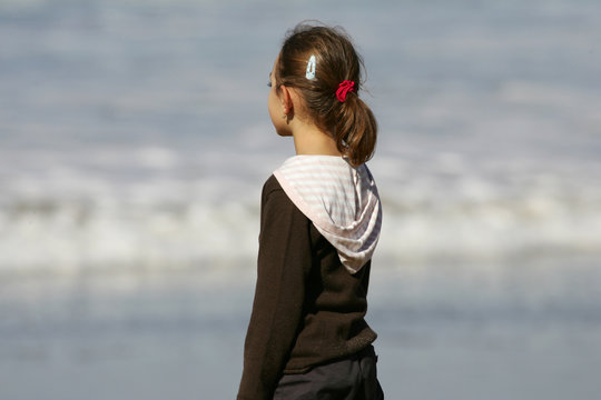 petite fille avec une queue de cheval qui regarde la mer