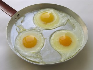 three fried eggs on an old alloy frying pan