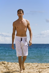 jeune homme séduisant debout marche sur la plage au soleil 