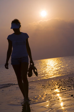 Girl walking along the coastline in sunset  