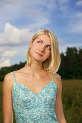Fototapeta na wymiar Beautiful blond girl in the field, blue cloudy sky behind her