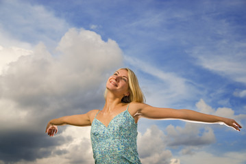Fototapeta na wymiar Beautiful blond girl with arms wide open over blue cloudy sky