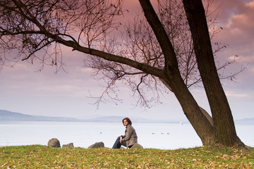 A young woman / lady is sitting and have a relax under a tree