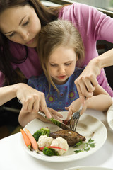 Obraz na płótnie Canvas Mom helping daughter cut food.