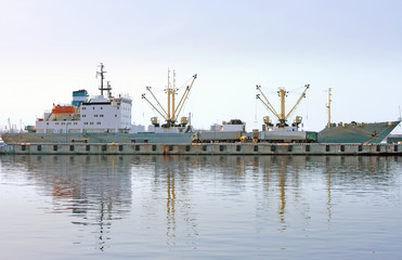  cargo ship docked and loading in port fully reflected in water