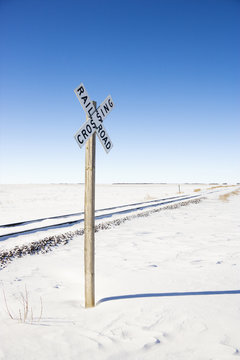 Railroad crossing sign by tracks in rural snowy landscape.