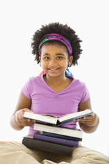 Girl with large stack of books smiling at viewer.
