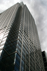 looking up a very tall steel office building with cloudy sky