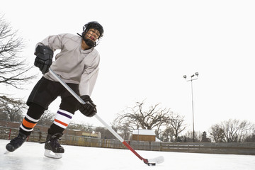 Boy in ice hockey uniform skating on ice rink moving puck.