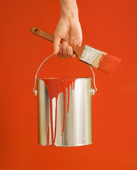 Caucasian female hand and leg holding paint can and paintbrush.