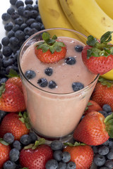 Smoothie surrounded by bananas, strawberries, and blueberries. 