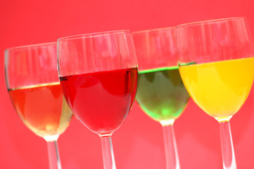 Glasses with drinks of various colours on red background