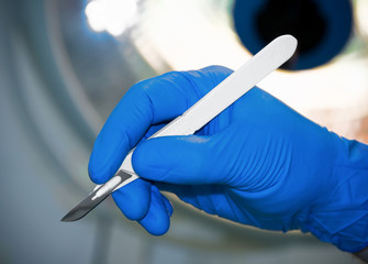 scalpel in surgeon's hand under lamp