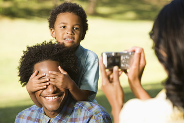 Woman photographing husband and son in park with camera.