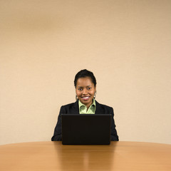 Businesswoman sitting at conference table typing on laptop.