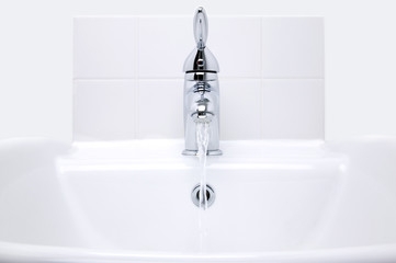 White modern ceramic handbasin and chrome tap, water running.