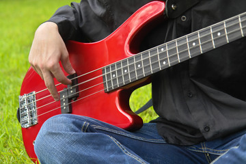 young man playing the bass guitar on the lawn