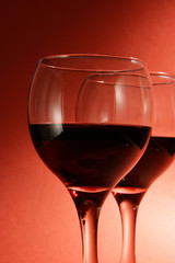 Two glasses of red wine over deep red background