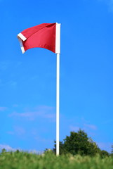 Red soccer corner flag against blue sky on green field