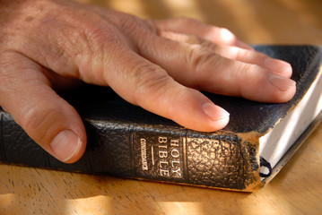 Hand On Well Used Old Bible Under Painted Light