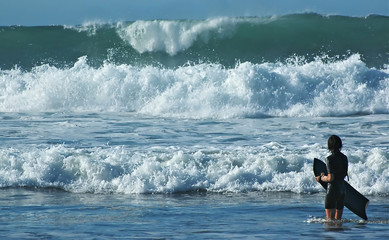 Girl with a bodyboard and dangerous ocean waves.