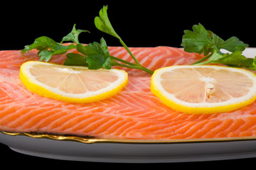red salmon with lemon and parsley on plate isolated on black