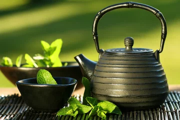Photo sur Plexiglas Theé Théière asiatique en fer noir avec des brins de menthe pour le thé