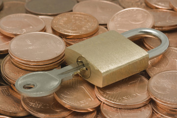 Padlock with key on top of a pile of coins