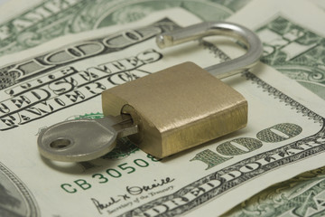 Opened padlock with key on top of hundred dollars bill