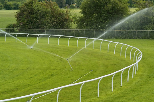Sprinklers watering a lush green racecourse,