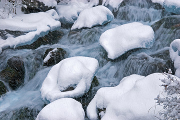 Winter mountain creek cascades during snowfall
