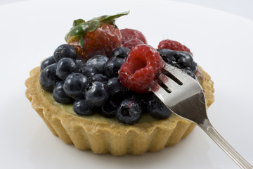 eating a tart with mixed berries, fork, white background