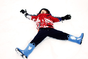 A happy kid playing in the snow as a snow angel