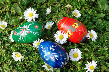 Obraz na płótnie Canvas Three painted easter eggs on grass with daisies