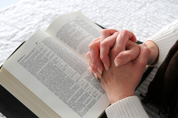 Woman's hands clasped in prayer over an open Bible © R. Gino Santa Maria
