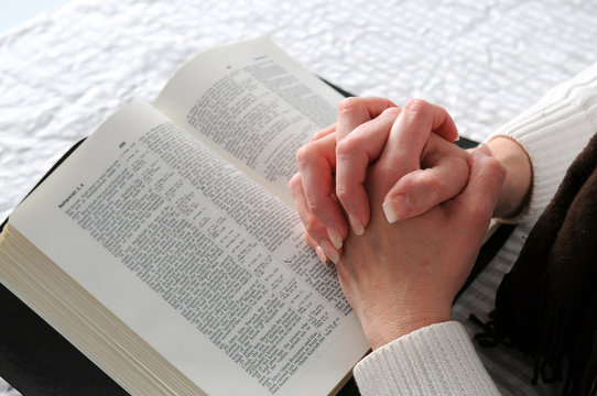 Woman's hands clasped in prayer over an open Bible
