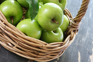 Cane basket of green Granny Smith apples, on rustic tabletop.