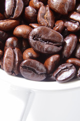 Close up of roasted coffee beans in a white cup.