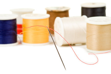 Sewing needle with various colored spools in background - obrazy, fototapety, plakaty