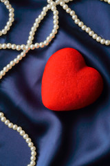 Pearls and red heart on a satin background